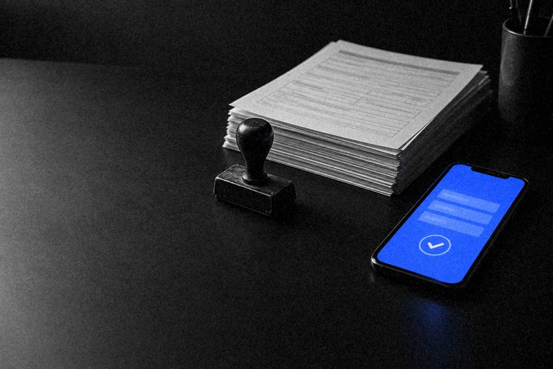 Стопка бумажных заявлений и печать рядом со смартфоном, на синем экране электронная форма с галочкой