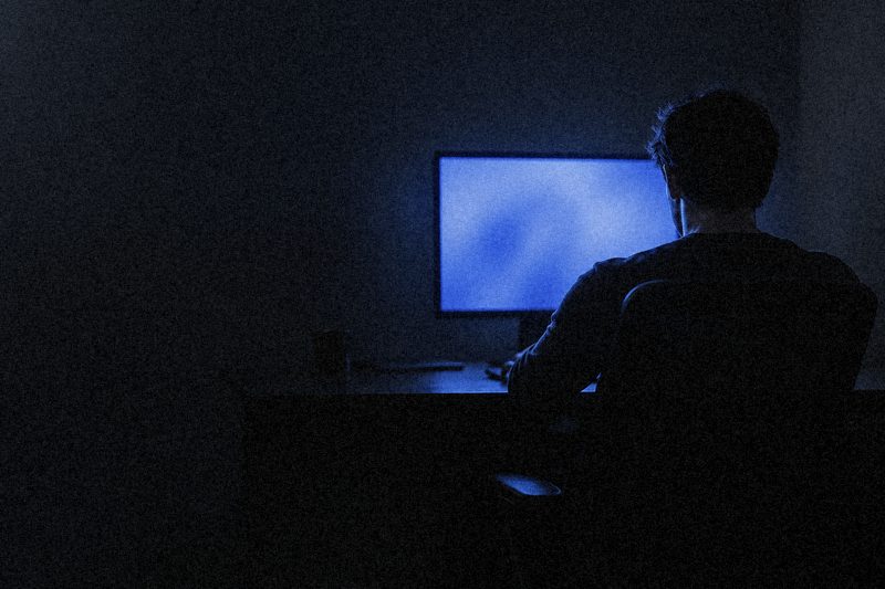 Разработчик ночью сидит перед монитором, экран светится синим