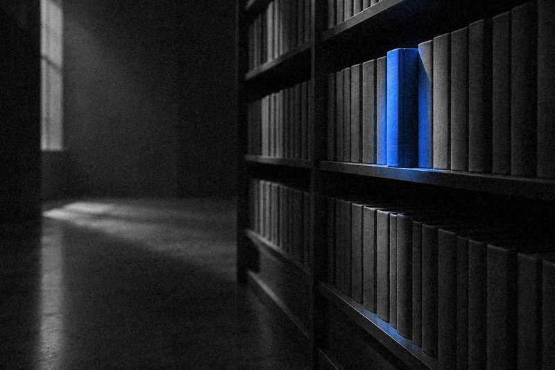Ряд одинаковых книг на полке, луч синего света выделяет одну выдвинутую книгу