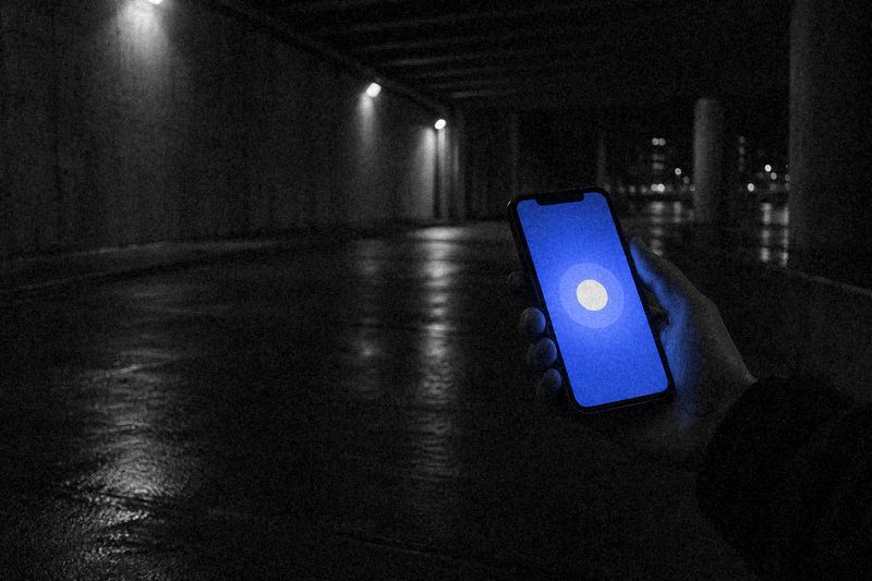 Рука держит смартфон с синим экраном и круглой кнопкой подключения в ночном подземном переходе